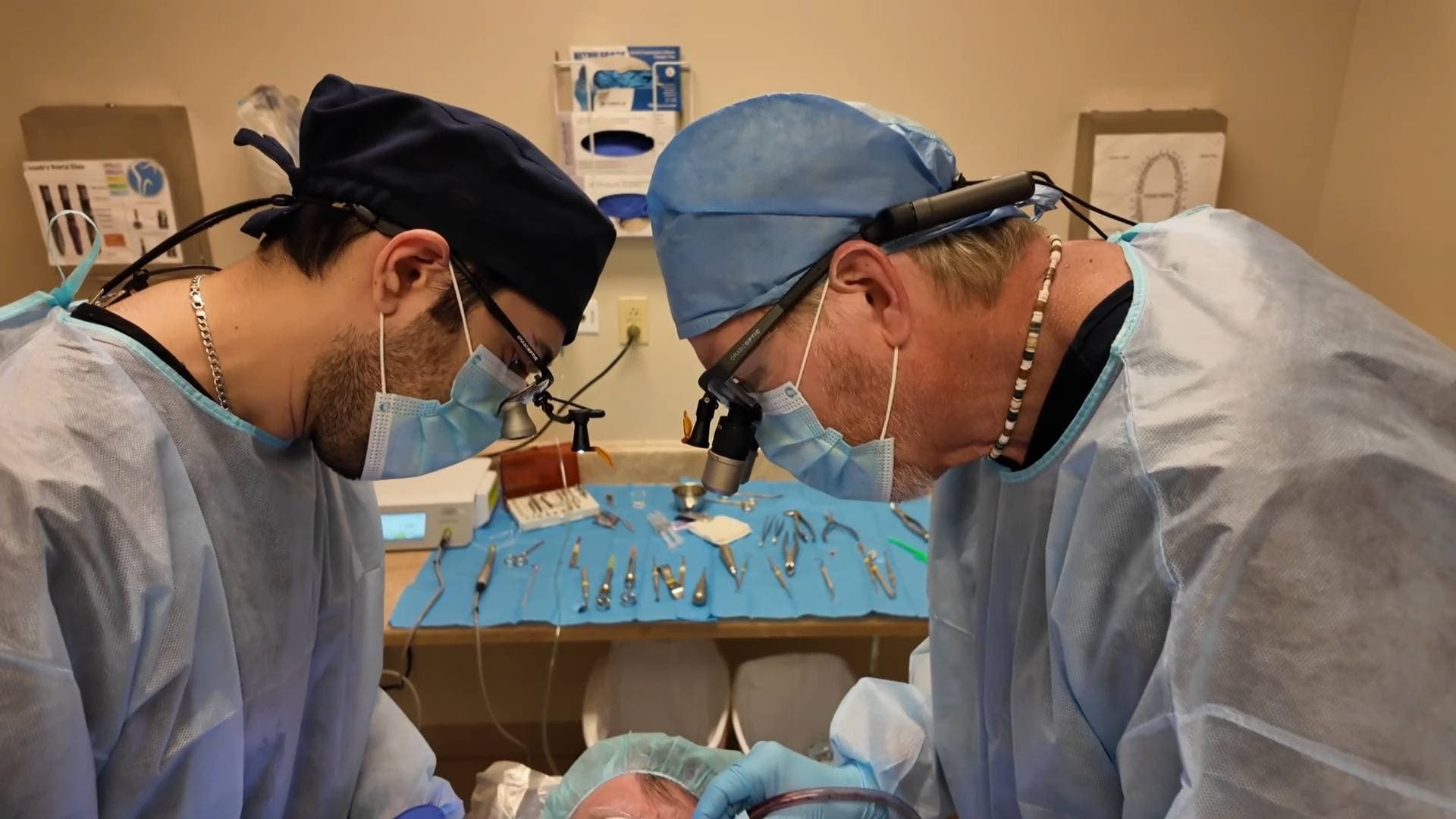 Dentists performing implant surgery on a live patient under supervision.